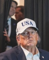 Zoom in on photo from article showing a tired Trump with white baseball cap marked USA