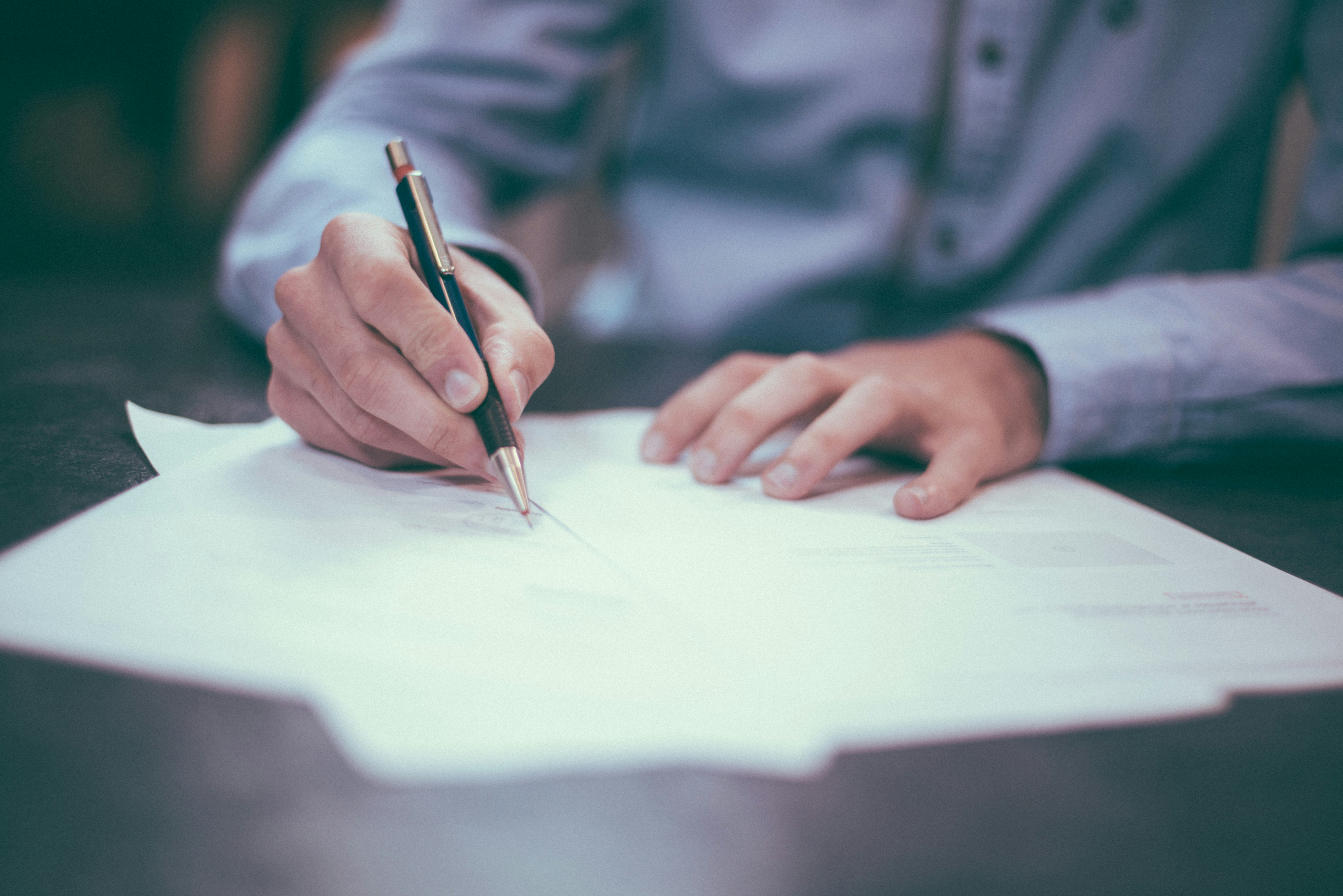 Persona con pluma en mano escribiendo sobre un escritorio