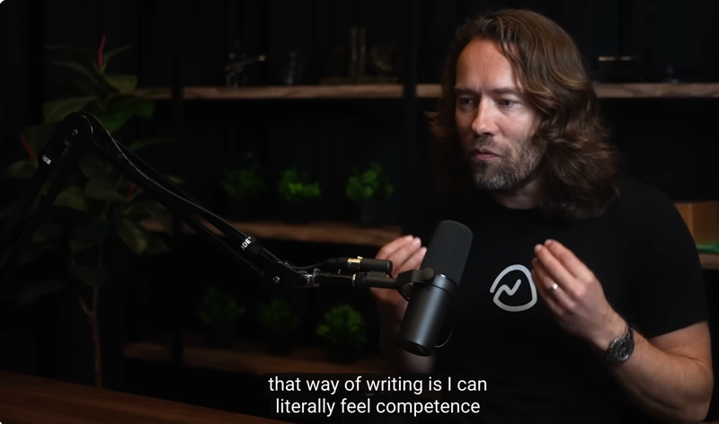 David Heinemeier Hansson, also known as DHH, speaks passionately into a microphone on the Lex Fridman Podcast. He gestures with both hands while wearing a black Basecamp t-shirt, seated in a dimly lit studio with shelves and plants in the background. Subtitle reads: "that way of writing is I can literally feel competence."