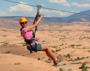 Smiling guest ziplining over red rock canyon in Moab Utah