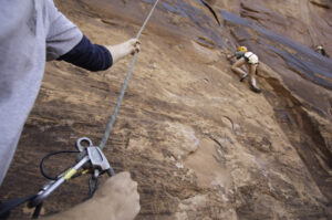 Certified climbing guide belaying guest on top rope system in Moab
