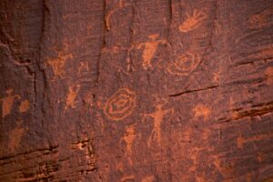 Ancient petroglyphs carved into red rock wall near Moab with horned figures and animals