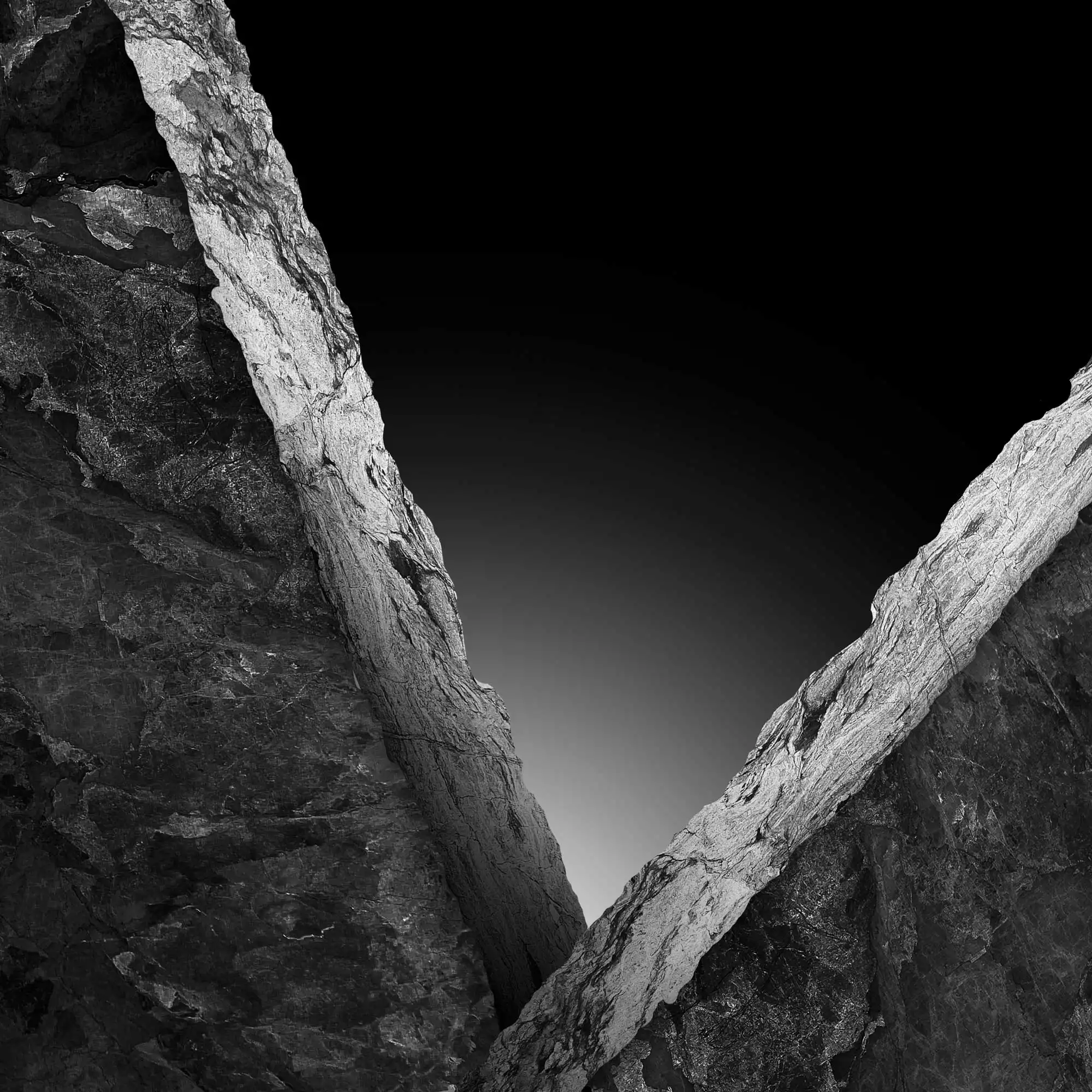Abstract view of a stark rock crevice against a dark sky, with the contrasting textures and edges highlighted in a monochromatic tone.