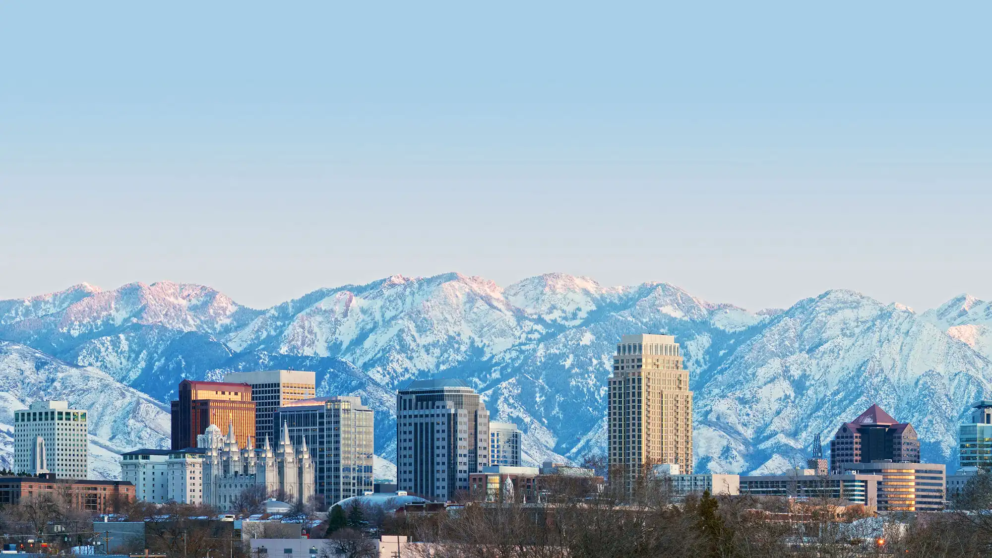 Panoramic view of Salt Lake City skyline with Utah State Capitol and the snow-covered Wasatch Mountain Range in the background during twilight.