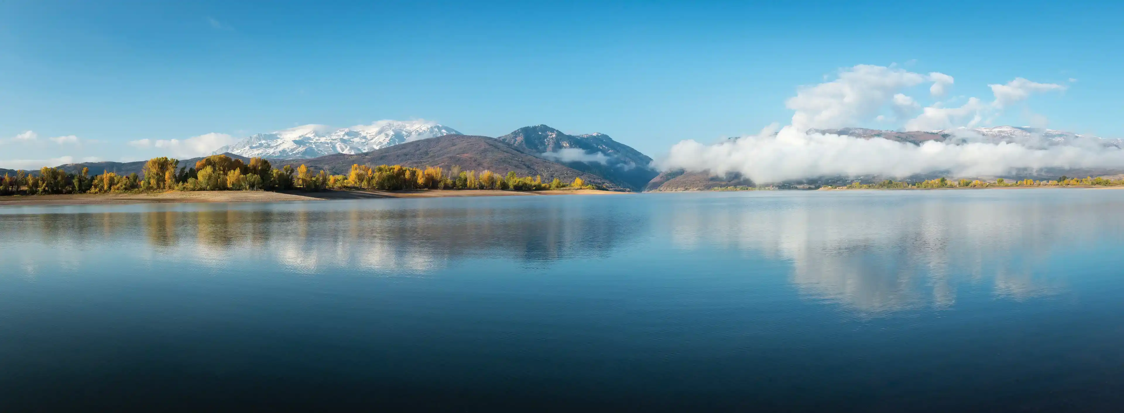 Pineview Reservoir in fall set against a snow capped Snowbasin Resort and mountainscape.