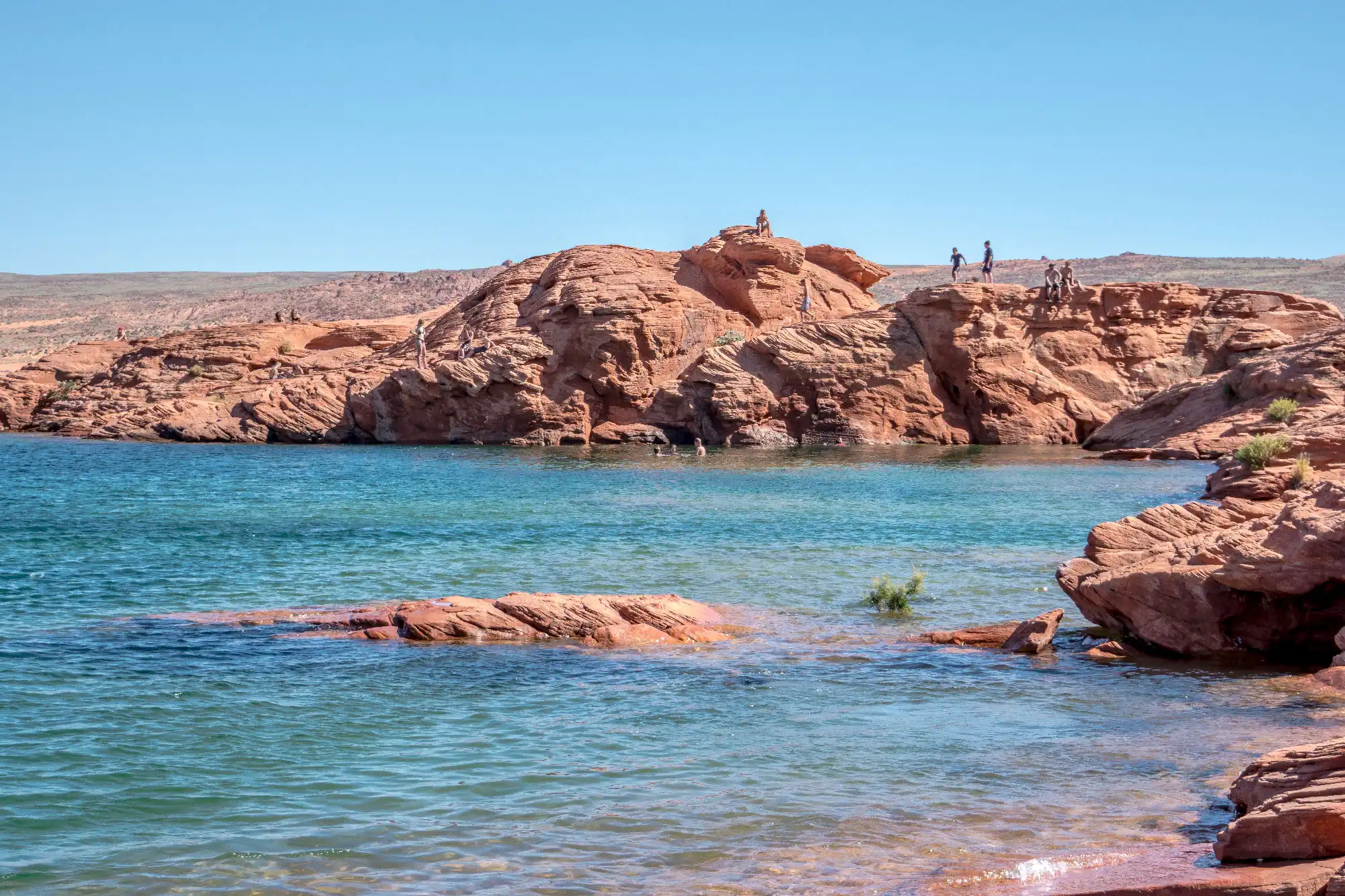 Swimmers standing along a ridge about to dive into the turquoise waters of Sand Hollow State Park