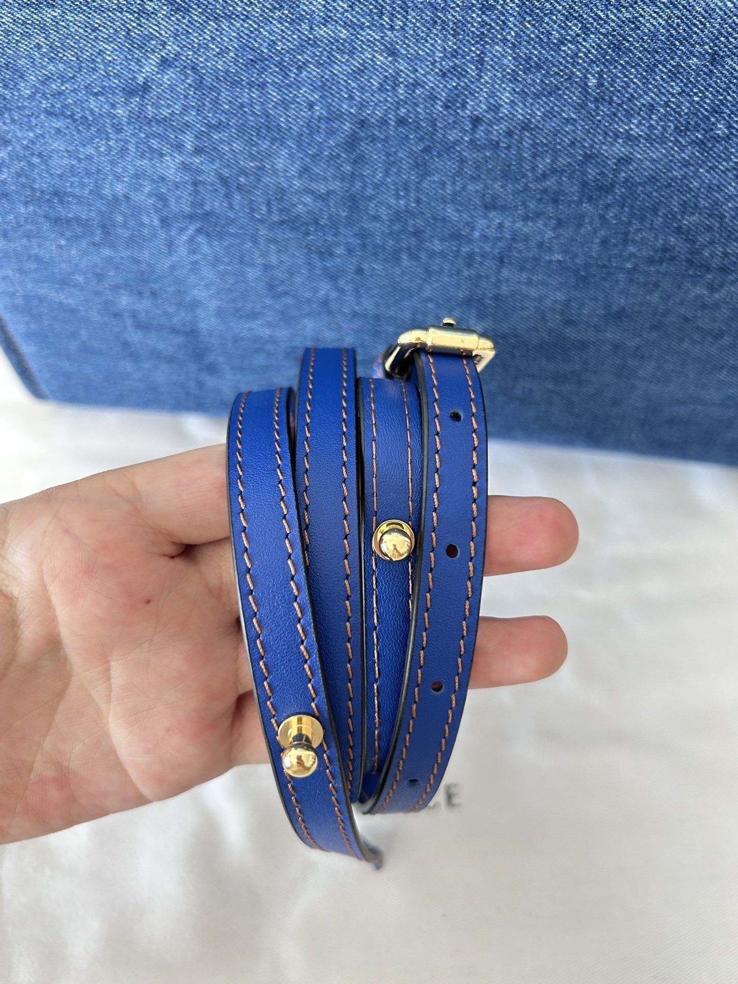 Versace Blue Leather Strap with gold hardware and contrasting stitching on a denim bag.