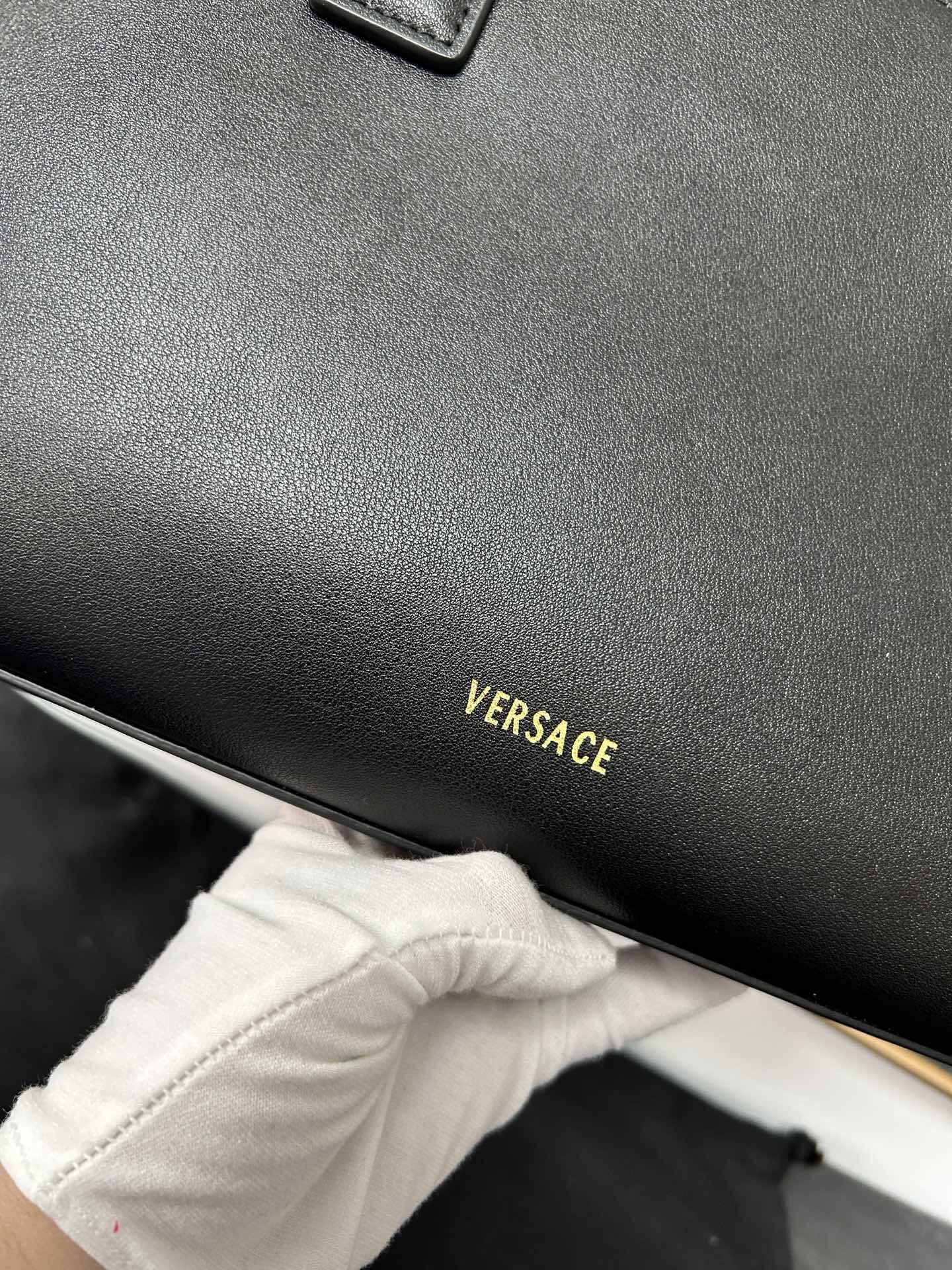 Versace Black Leather Tote with gold logo, premium quality, held by a gloved hand.