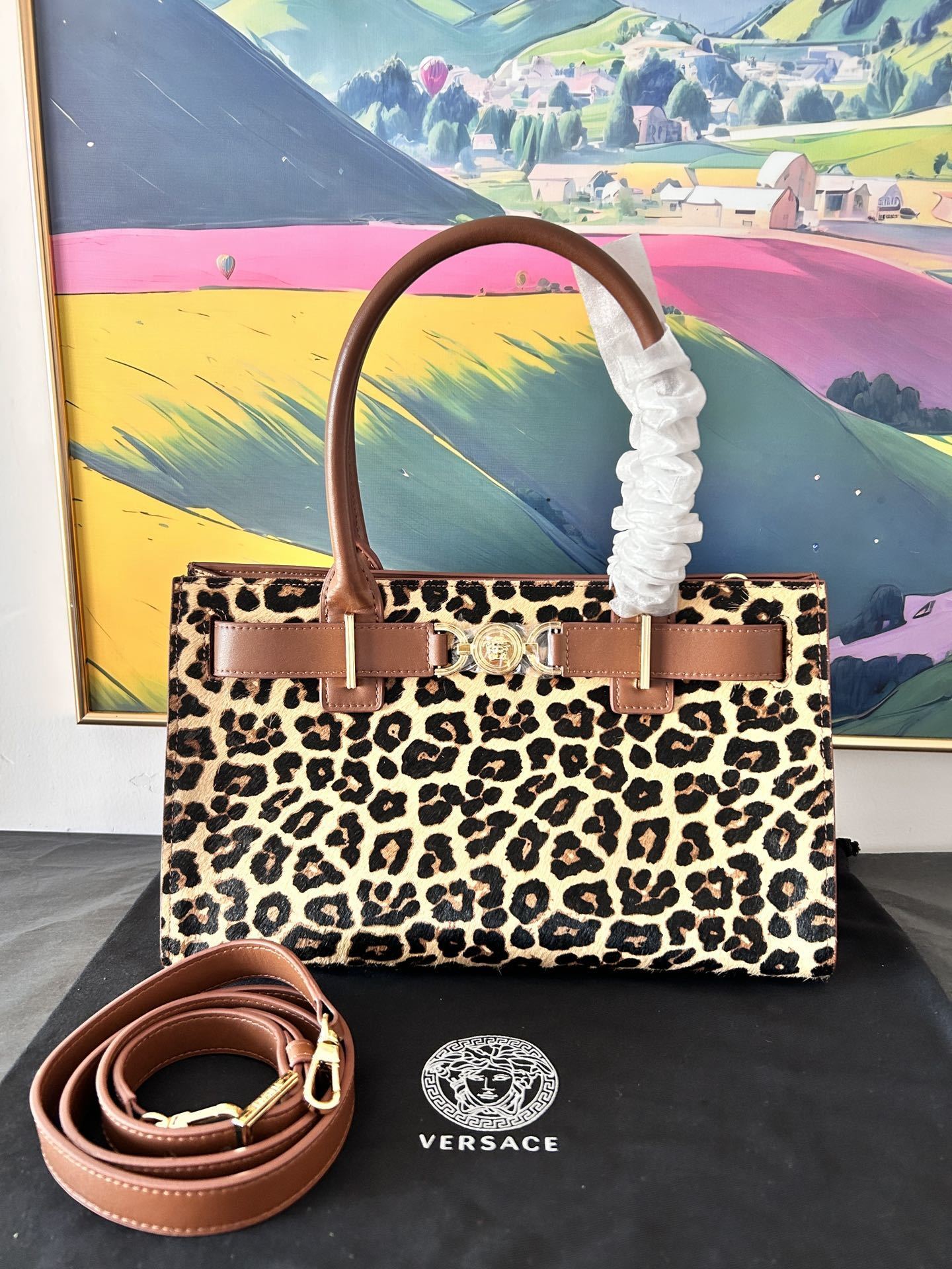 Versace Leopard Tote Bag with brown leather handle and gold Medusa hardware on a dust bag.