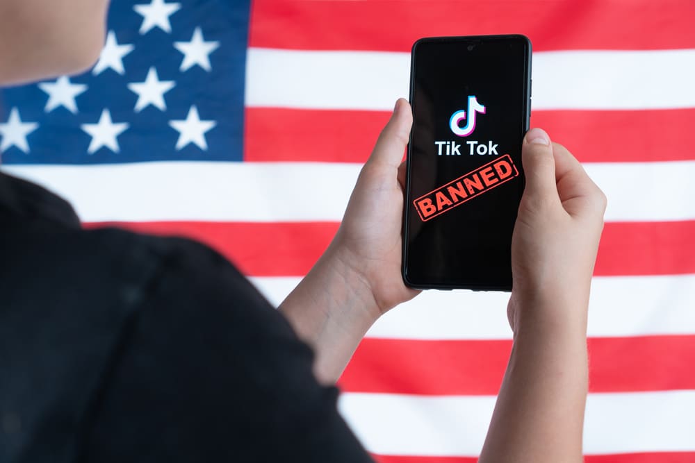 a teenager holds a smartphone with the tiktok logo and against the background of the american flag. selective focus. donald trump to ban tiktok in united states. russia, kazan august 08, 2020