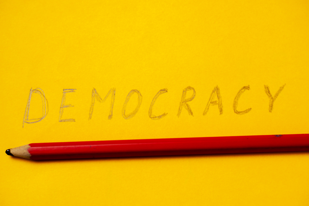 the word democracy written in pencil on a yellow background.