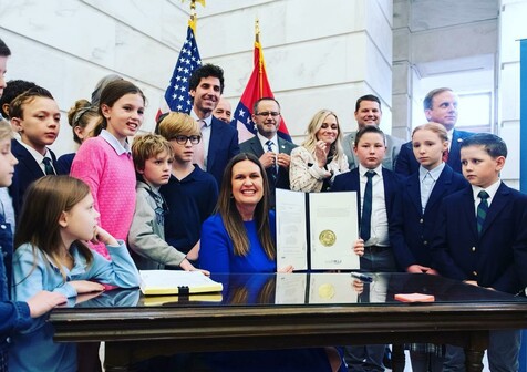 Governor of Arkansas and former mouthpiece of Sauron, Sarah Huckabee Sanders, signing a law in March 2023 eliminating permits that required employers to verify a child’s age and their parent’s consent. Without work permit requirements, companies caught violating child labor laws can more easily claim ignorance. She is surrounded by children looking mostly sad, confused, or despondent. Three young chaps on the right dressed in little business suits think they’re going to go work on Wall Street now, but even they don’t seem happy about it.