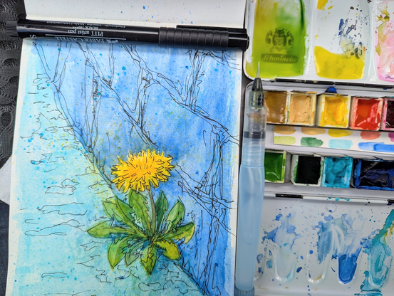 Open sketchbook page with a watercolor painting of a single bright yellow dandelion growing on a wall. Next to it a watercolor paint box and brushes. by Karen Kaspar