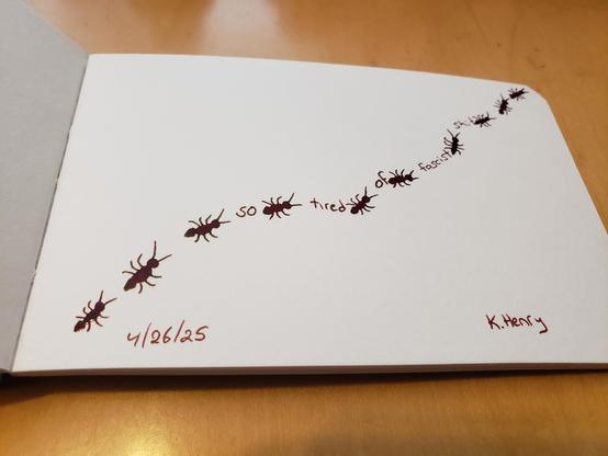 Hand drawn generative/procedural art in ink on an open page of my sketchbook. The abstract pattern looks like ants crawling along a wavy path across my sketchbook. There are words between the ants that read "so tired of fascist shit".