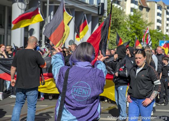 eine person zeigt mit beiden händen mittelfinger richtung der nazidemo