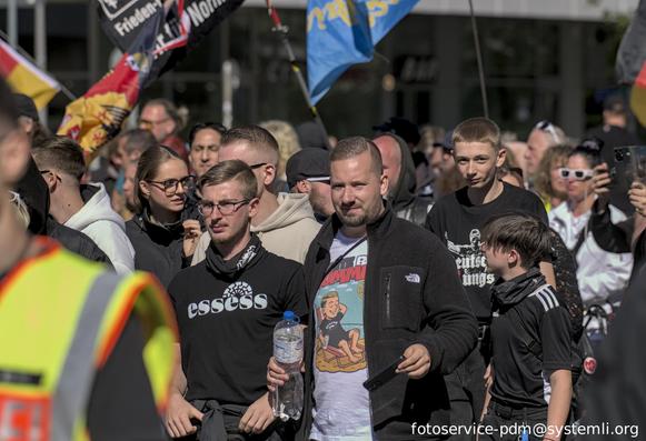 nazidemo, ein teilnehmer trägt ein schwarzes shirt mit schwarzer sonne und aufschrift "essess", danben ein teilnehmer mit offener jacke und drunter ein shirt "wihte boy summer" mit schwarzer sonne und person auf liegestuhl