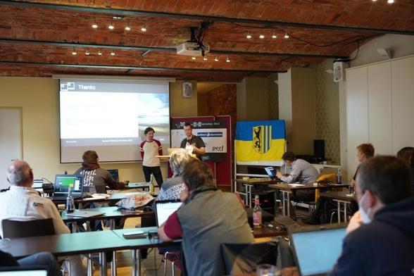 Conference room with 2 people speaking. Flag of Leipzig on the right side of the stage