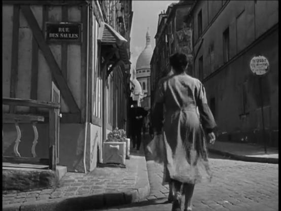 Scene from Berlin Express. A portly matron walks away from the camera up a narrow, cobblestoned street, with a glimpse of Sacré-Cœur at the end. A gendarme is coming down the street from the opposite direction. The Tudor-styled building at left has changed since 1948, but the distinctive pattern of the walls on the right identify the street as Rue Saint-Rustique.