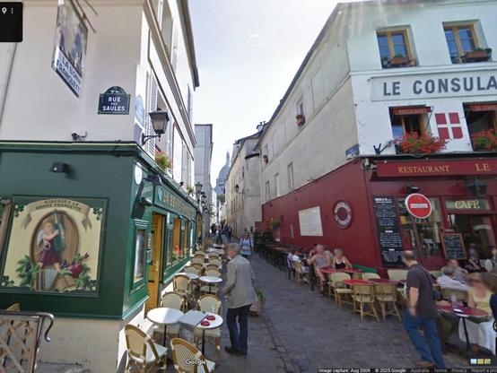 2009 Google Street View of the spot. The building at left (La Bonne Franquette) has changed but the wall at right (Le Consulat) is recognisable from the movie scene, as is the rounded shoulder of the building beyond it. The angle of Sacré-Cœur at the end of the alley also looks right. The cobbled paving has changed.