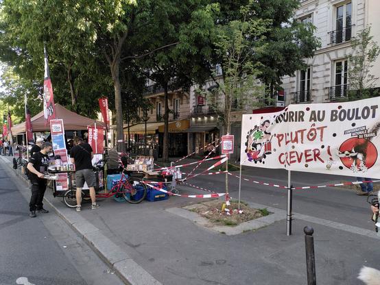 Stand du syndicat du bâtiment dans une rue parisienne barnum drapeaux rouge et noir une banderole "mourir au boulot ? Plutôt crever !"