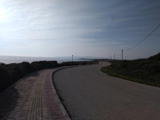 Coastal road snaking into the distance. Beyond across the sea is low-lying mand rising up from the water.