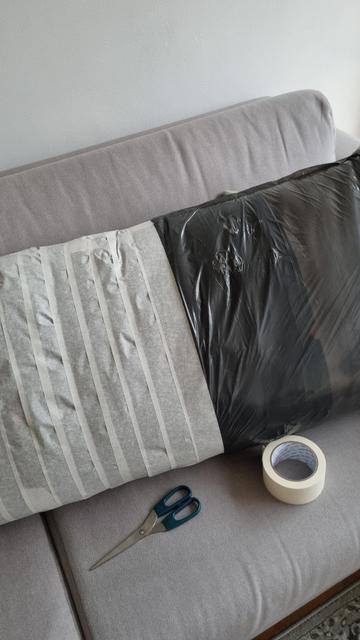 Covering a grey sofa pillow with a layer of a plastic bag and a masking tape