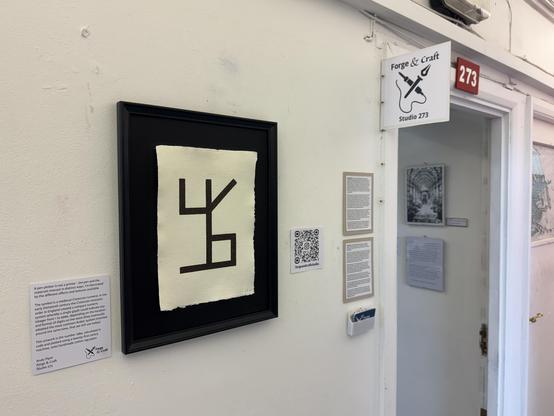 A large Cistercian glyph plotted on rough cotton paper on a dark frame. It is hanging on a wall outside an open studio door. The studio title is Forge & Craft and the number is 273.