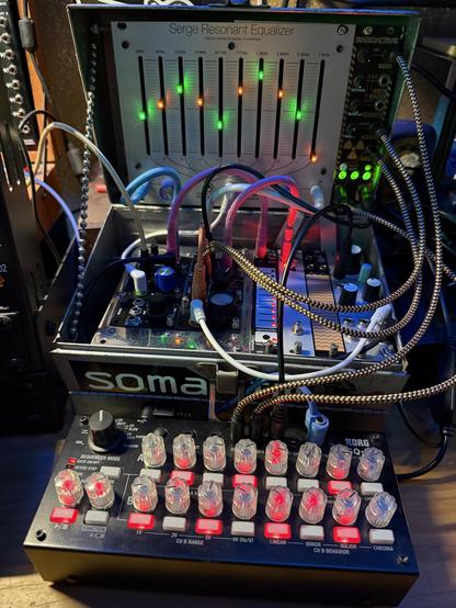 Electronics in three layers, rows of LED lit knobs, wires extending across modules and lit from underneath. The small synth case is no bigger than a lunchbox.