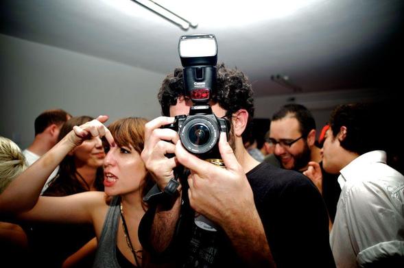 Privacy issues in meeting apps: photograph of a crowd of people indoors with a photographer pointing his camera directly towards the viewer. Photo attribution: Flickr user michellzappa