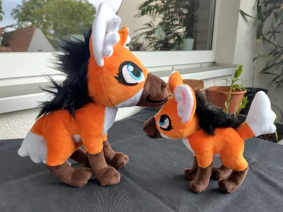 A larger and a smaller orange maned wolf plushie put next to each other. Too different size for nose kiss but they still look cute with one kissing the other's forehead.