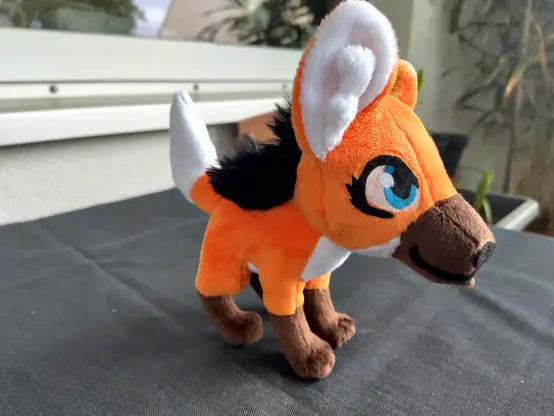 A small maned wolf plushie standing on dark grey table cloth looking illegally cute.