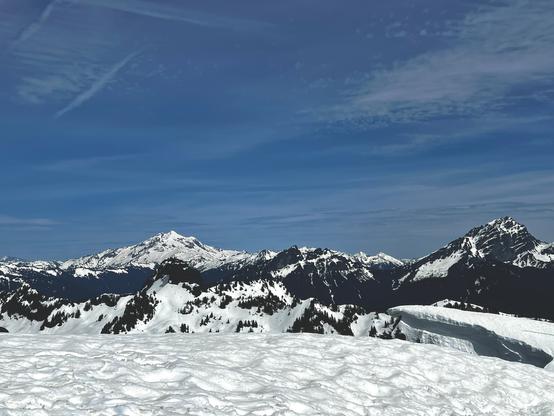 View of Glacier Peak, an immense, 10,000+ ft mountain from the top of Dickerman, and several other peaks to the right which are nearer. The foreground is all snow.