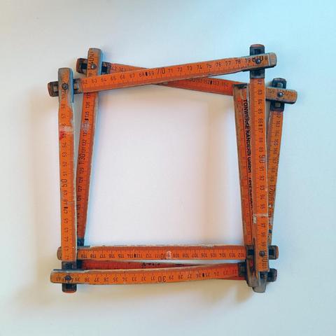 A heavily worn orange wooden folding metre rule on a white table. The links are all folded out to form a kind of square.