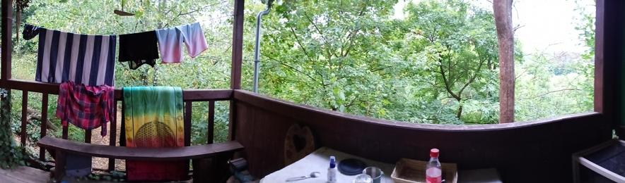 A panorama photo of a wooden cottage terace With trees in background.