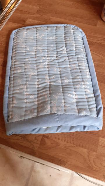 The reverse of the hot water bottle cover. A pale blue fabric with a white pattern of leaves and birds on it is quilted in long lines. Teh edge is bound in pale blue