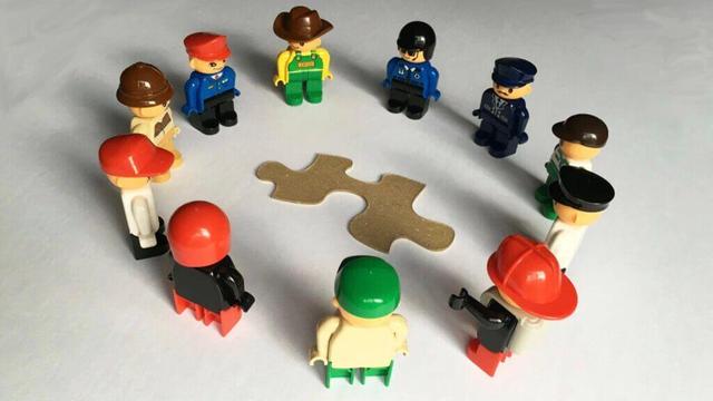 A photograph of a circle of standing Lego people surrounding a jigsaw puzzle piece Image attribution: Wikimedia Commons under the Creative Commons Attribution-Share Alike 4.0 International license