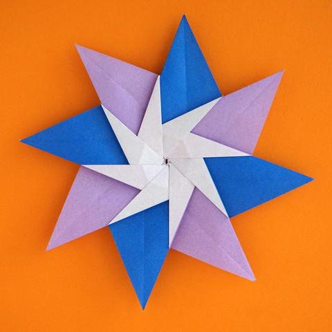 An eight-piece origami star made from blue and lilac paper on an orange background. White paper for an eight-pointed pinwheel in the centre of the model.