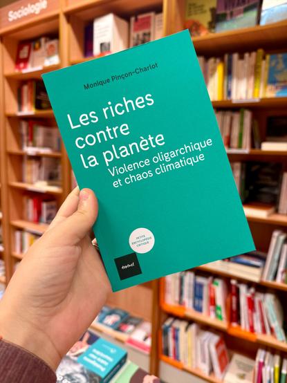 Livre pris en photo devant un mur d’étagères pleines de livre. La couverture est verte avec le titre en blanc.