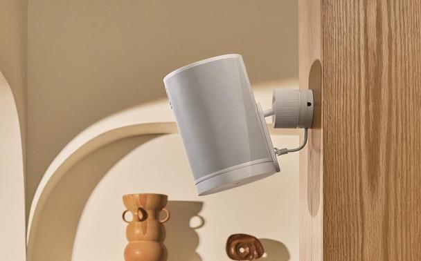 Ein weißer Sonos-Lautsprecher ist mit einer Halterung an einer Holzwand befestigt. Foto (c) Sonos.