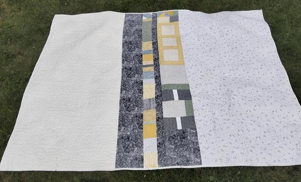 the reverse side of the quilt, it is light colored, strips of grey and yellow running down the center of it
