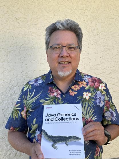 Stuart Marks, wearing a blue aloha shirt with flowers, holds a copy of the book “Java Generics and Collections, second edition” by Maurice Naftalin and Philip Wadler, with Stuart Marks. There is a picture of an alligator on the front cover.