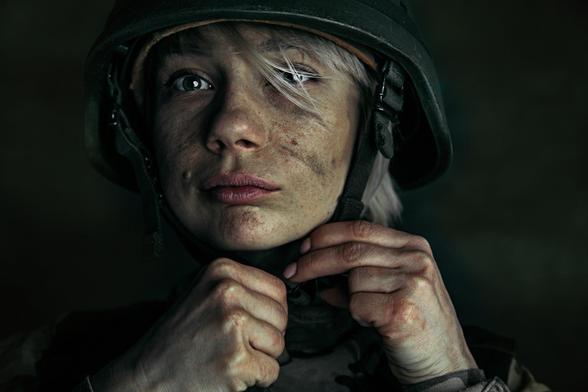 Women with wide eyes covered in dirt putting on an army helmet.