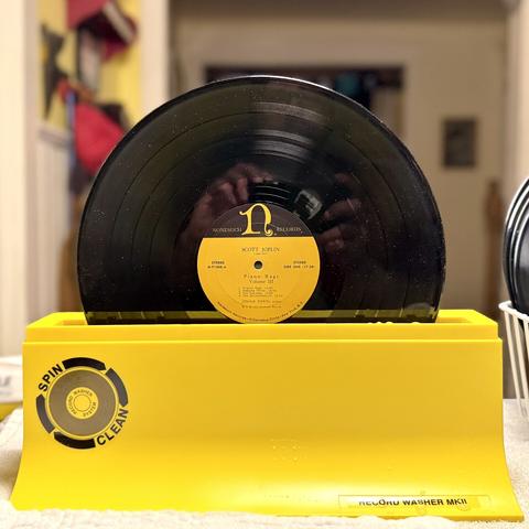 An LP of Joshua Rifkin's "Piano Rags by Scott Joplin Volume III" on Nonesuch Records sitting in a bright yellow plastic device labeled "Spin Clean Record Washer MKII"