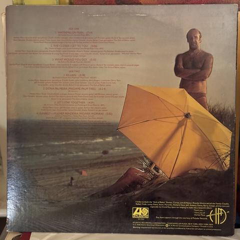 The back cover of Herbie Mann's "Sunbelt," still on the beach with a Herbie Mann standing behind an umbrella, wearing a speedo and glistening in the sun