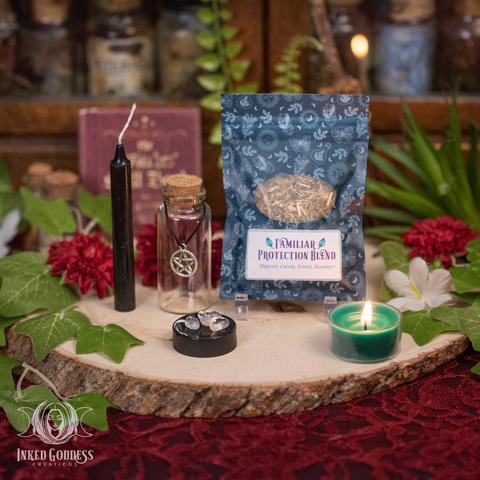 The contents of our Familiar Protection Mini Witch Bottle Kit are arrayed on a raw wood slice. A black mini chime candle stands next to an empty clear glass vial. The vial has a cork stopper, and there is black thread hanging loosely around its neck with a silver pentacle charm. The Familiar Protection Blend of herbs (mugwort, catnip, fennel, and rosemary) stands behind a small pile of three tiny clear tumbled quartz nuggets. This is an exclusive product from Inked Goddess Creations.