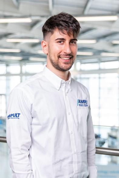 A photo of Gianmarco looking happy, wearing a white shirt with the AMRC logo on it.