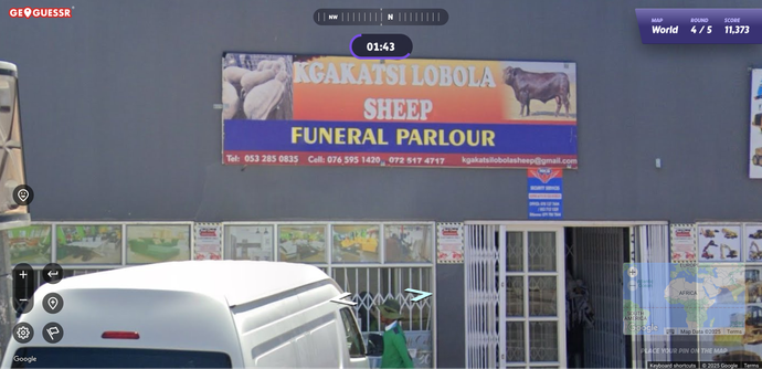 A screenshot from Geoguessr (that uses Google Streetview) somewhere in South Africa showing a business sign that says "Kgakatsi Lobola Sheep Funeral Parlour" with a picture to the left of some sheep and a photo to the right of a rather large cow.