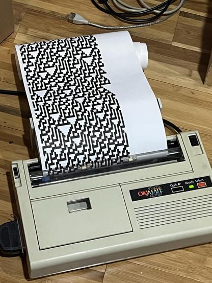 A beige printer with continuous paper spooling out of it with the rule 30 pattern printed about 3/4 across the width of the page in bold black characters.