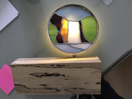 Circle of stainless steel, in it a piece of Tiffany with Iceland theme (waterfall). It has backlight. A piece of wood is placed underneath, not attached yet.

All is lying on a table.