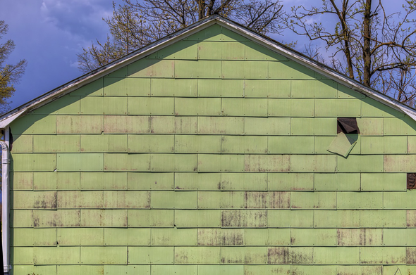 A weathered green wall with a missing piece reveals the aged character of a building.